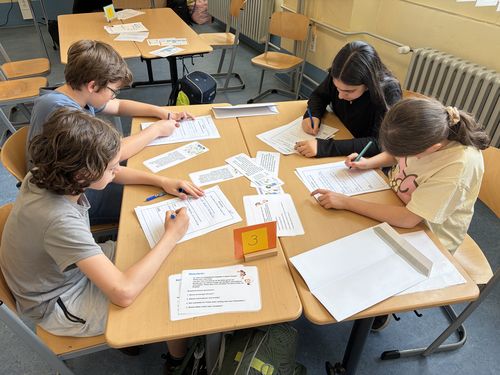 Vier Grundschüler*innen sitzen um einen Tisch herum im Klassenzimmer und bearbeiten gemeinsam eine Aufgabe.