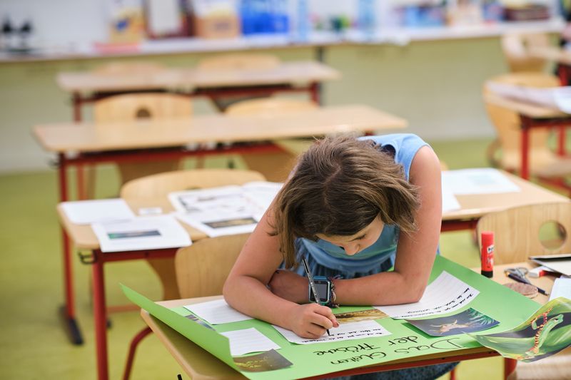 Eine Schülerin sitzt im Klassenzimmer an einem Tisch und schreibt auf ein Poster.