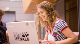 Eine Schülerin sitzt am Laptop und lächelt.