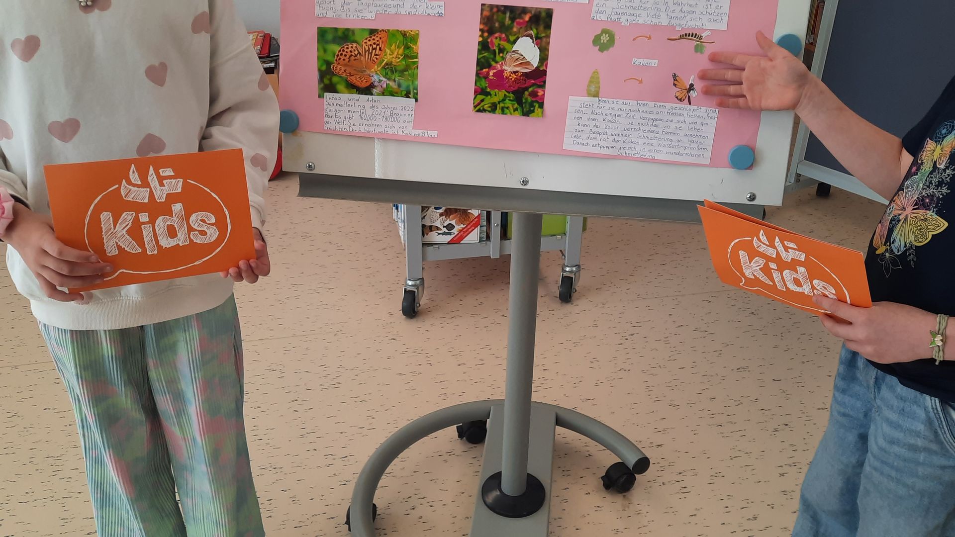 Zwei Grundschülerinnen halten orangene Karten auf denen "JP Kids" steht.