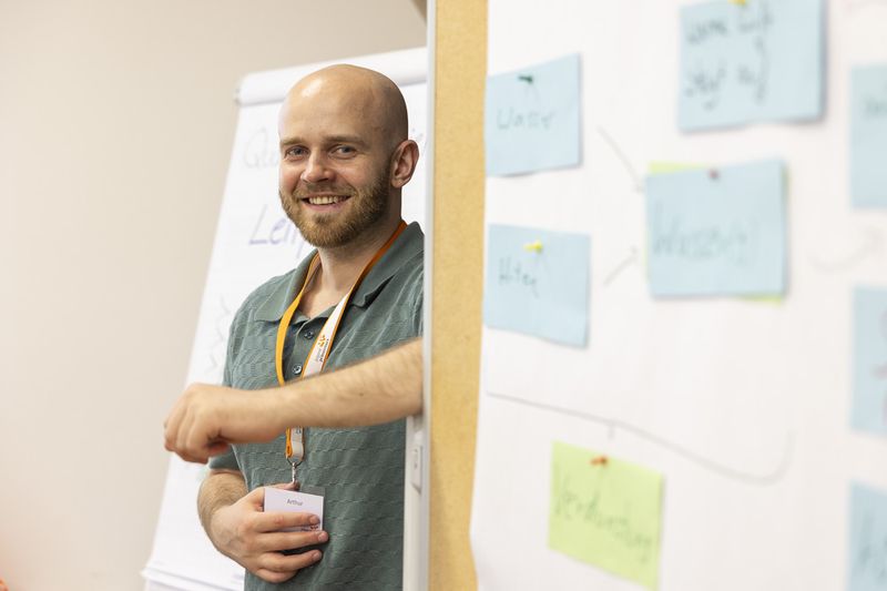 Ein Juniortrainer steht vor einer Flipchart, an der verschiedene Post-its kleben.