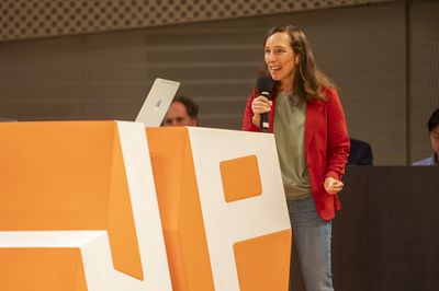 Eine Frau mit Mikro steht hinter einem großen JP-Pult