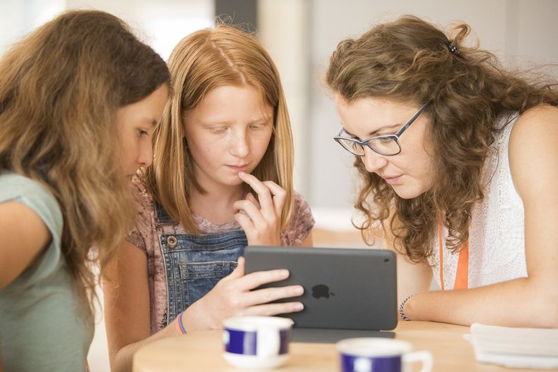 Zwei Schüler*innen und ein*e Lehrer*in schauen in ein Tablet.