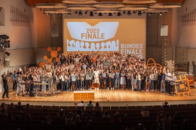 Eine Bühne ist gefüllt mit Menschen, die freudig ihre Arme in die Luft heben.