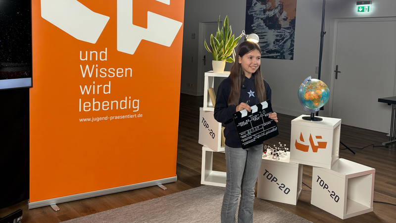 Schülerin hält eine Filmklappe beim Top-20-Dreh in der Hand.