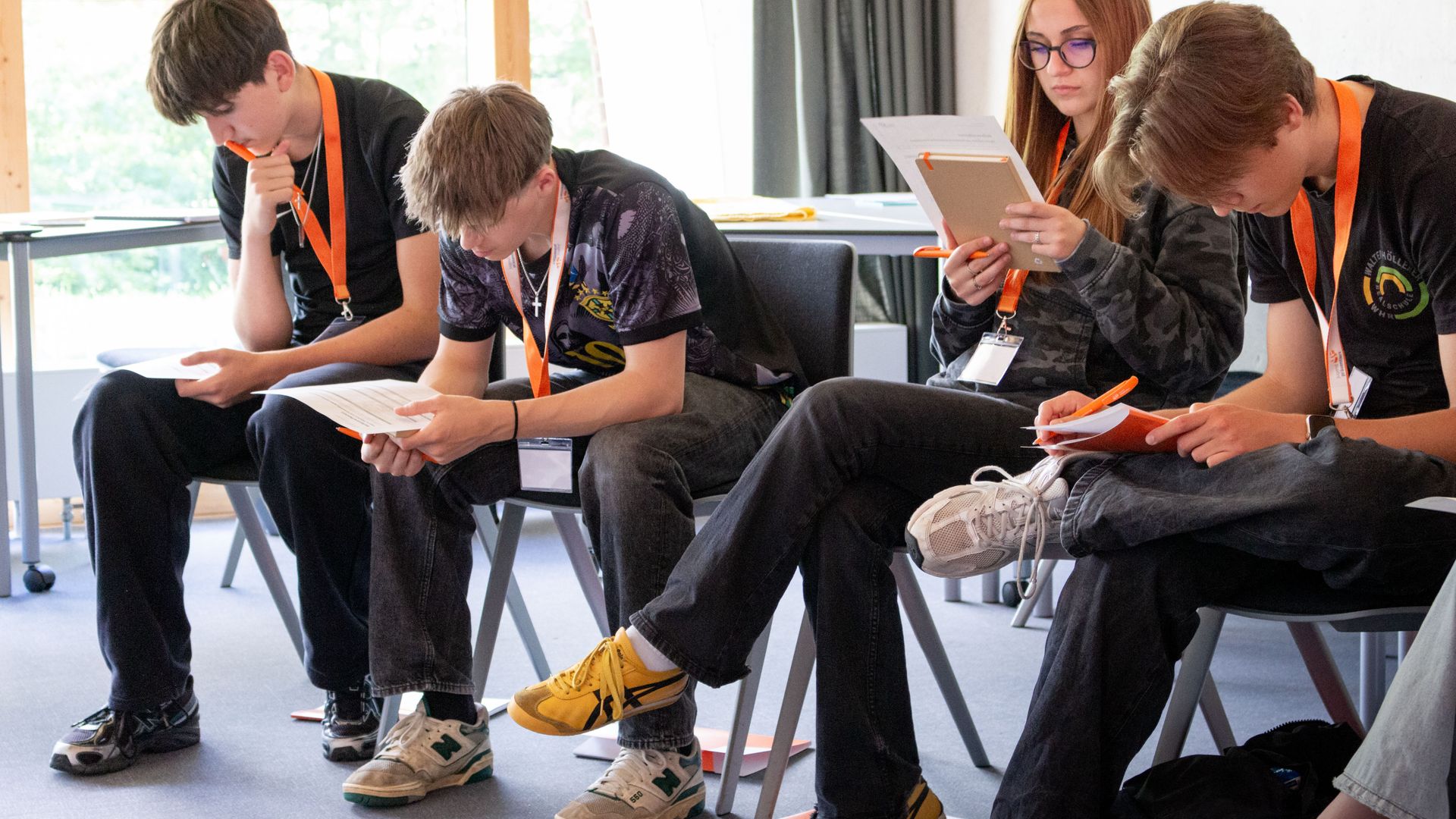 Drei Schüler sitzen nebeneinander in einem Seminarraum, sie tragen organgene Schlüsselbänder.