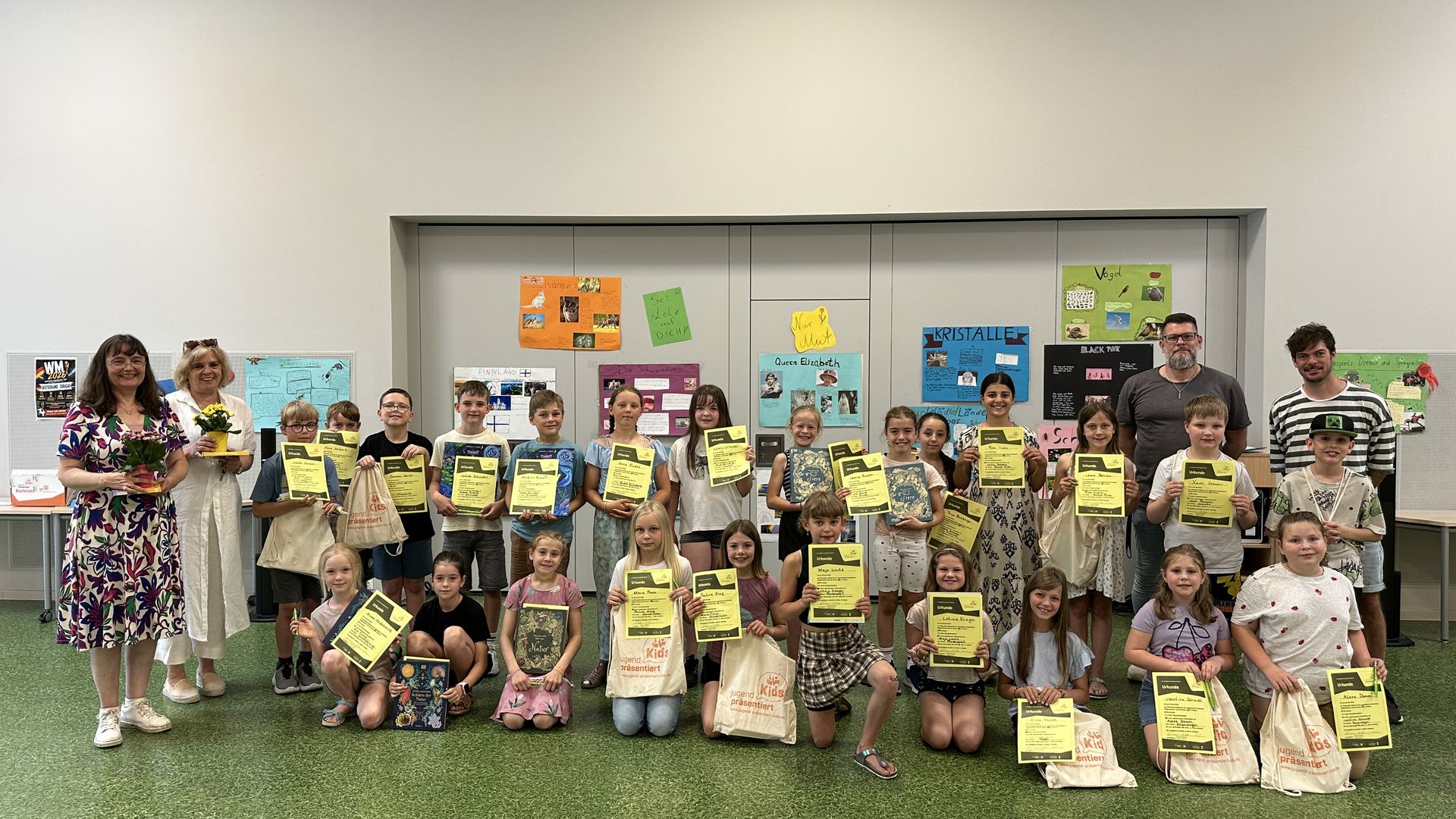 Eine große Gruppe von Grundschulkindern mit Lehrkräften blickt stolz in die Kamera und zeigt die Urkunden.