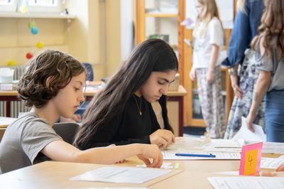 Zwei Grundschüler sitzen an einem Tisch im Klassenzimmer und blicken konzentriert auf ihre Arbeitsblätter.