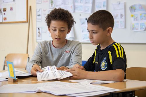 Zwei Grundschüler sitzen im Klassenzimmer an ihrem Tisch und blicken konzentriert auf ihre Arbeitsblätter.