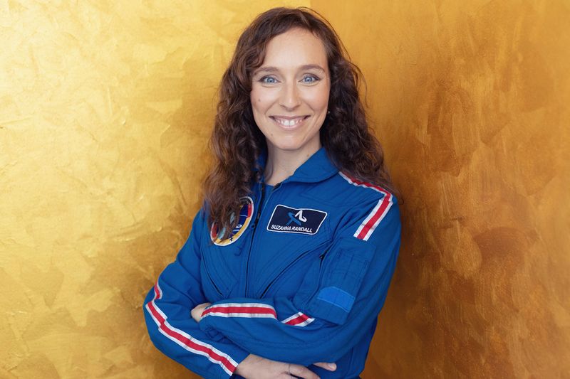 Eine dunkelhaarige Frau in einem Austronautinnen-Anzug lächelt in die Kamera